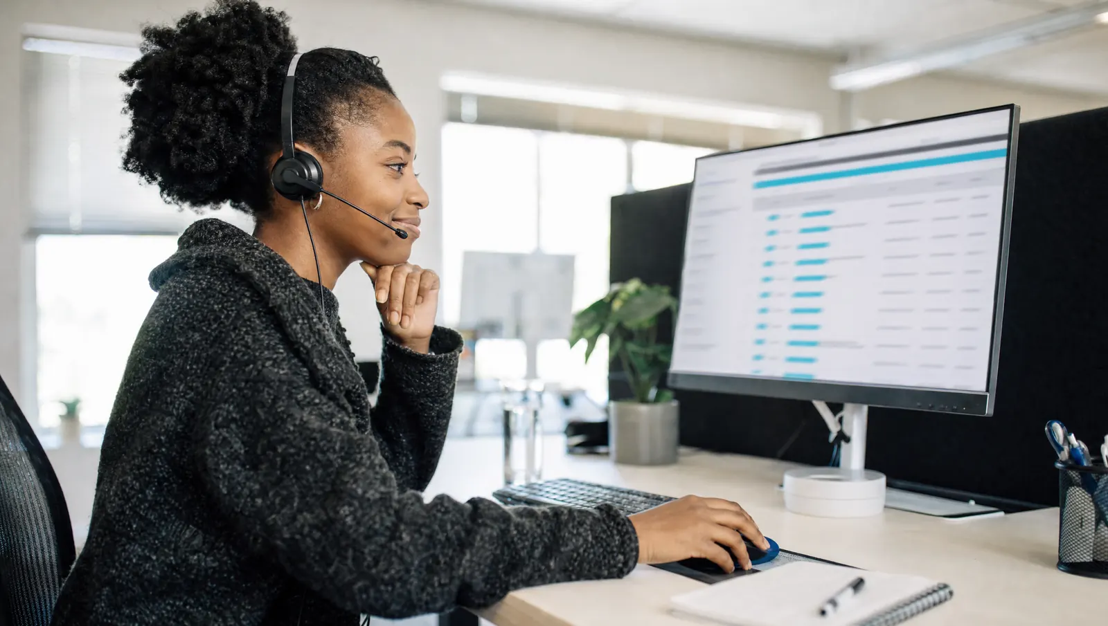 A young South African woman support engineer wearing a headset, looking at a list of helpdesk tickets on her screen
