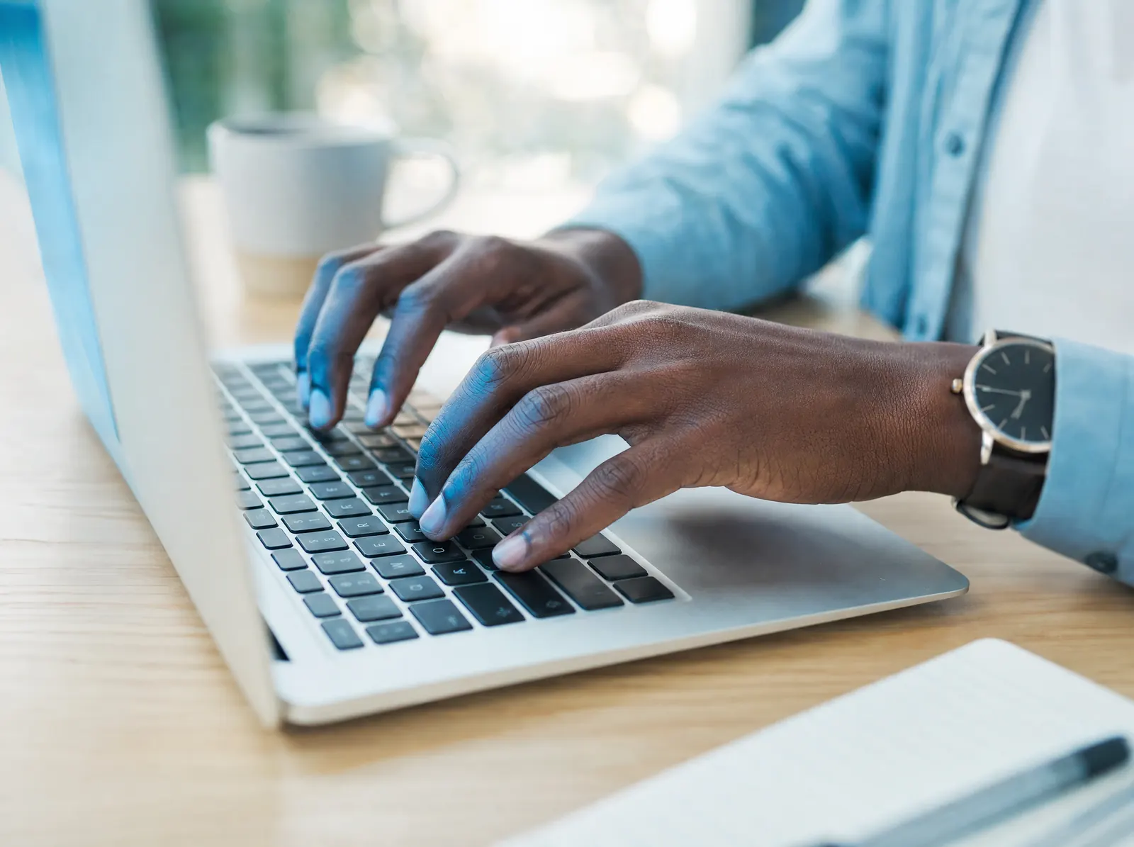 Hands typing on a laptop in soft morning light.